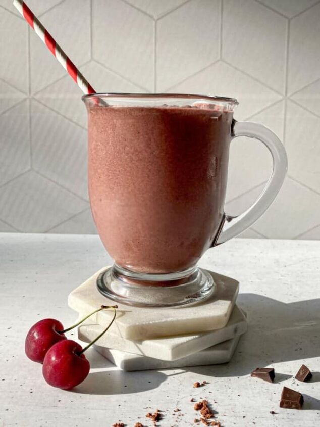 blueberry protein shake, Chocolate Cherry Smoothie in a glass with a straw Cherries a dusting of cacao powder and chocolate chucks are around the glass