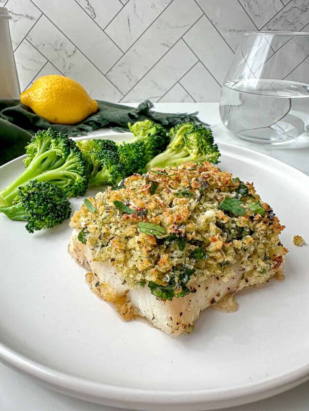 baked panko crusted cod, Parmesan panko crusted cod on a plate with broccoli A green towel glass of water and lemon are in the background