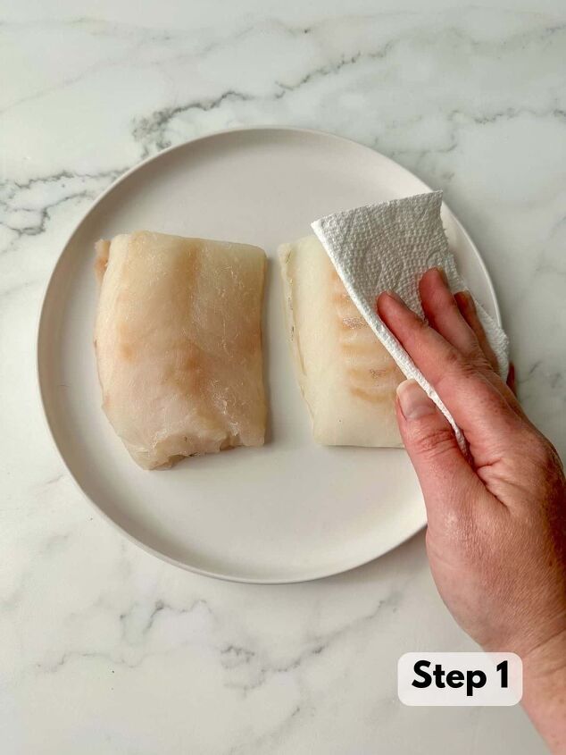 baked panko crusted cod, A hand drying fish with a paper towel Two fish on a white plate on a marble table