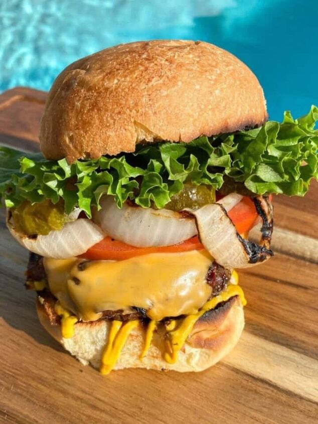 southwest burger with chipotle mayo, Grilled cheeseburger with all the toppings on a cutting board in front of a pool Beef burger with onions tomatoes pickles lettuce and mustard