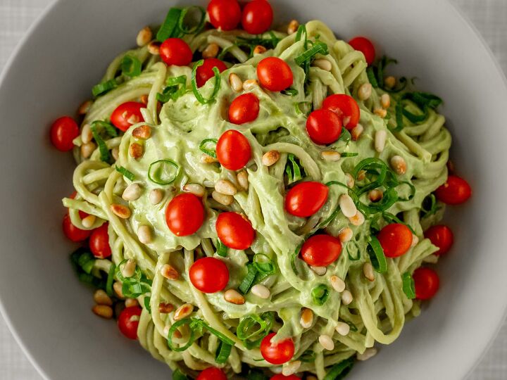 vegan avocado pasta, Close up of creamy avodado pasta vegan seen from top topped with pine nuts cocktail tomatoes and spring onions