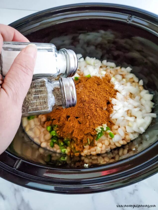 slow cooker chicken chili with white beans, chili seasoning and salt and pepper being added to crockpot
