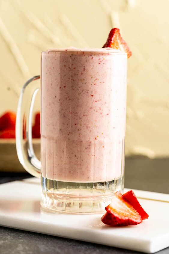strawberry banana milkshake, a glass full of milkshake sitting on a white marble plate