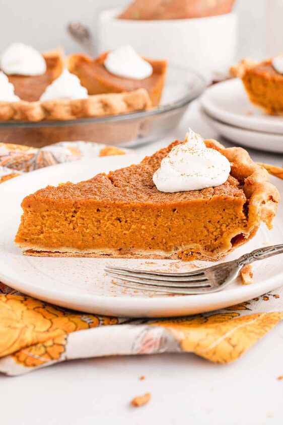 southern sweet potato pie recipe, A piece of southern sweet potato pie topped with a dollop of whipped cream on a white plate with the full pie in the background