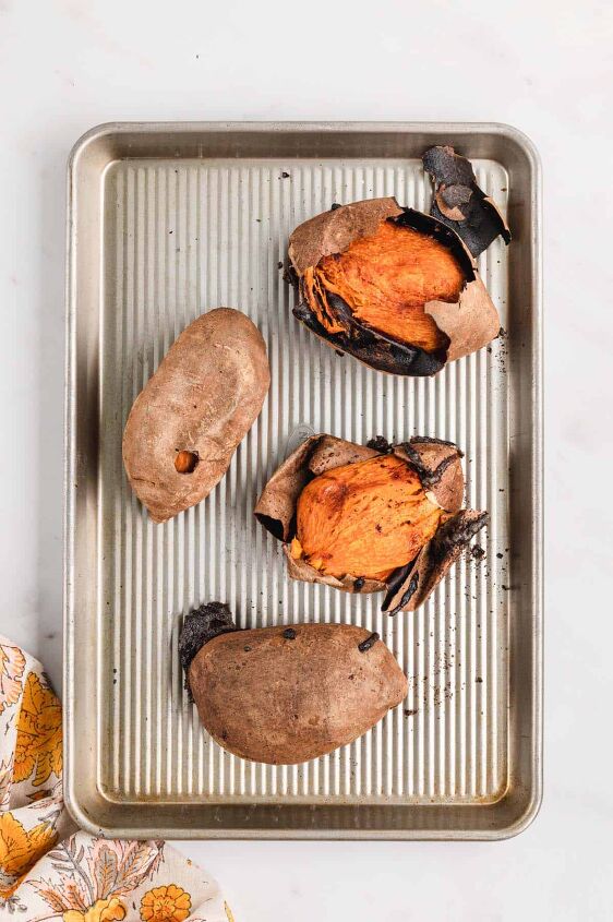southern sweet potato pie recipe, Four baked sweet potatoes on a sheet pan with the skin peeling off two of them on a white counter