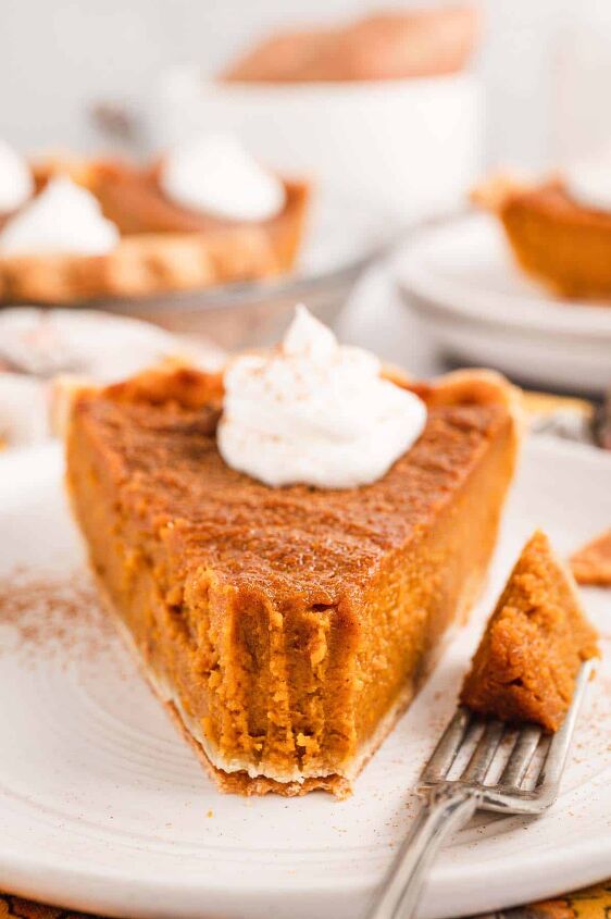 southern sweet potato pie recipe, A piece of sweet potato pie topped with a dollop of whipped cream on a white plate with a fork on the side with a bite of the pie on it