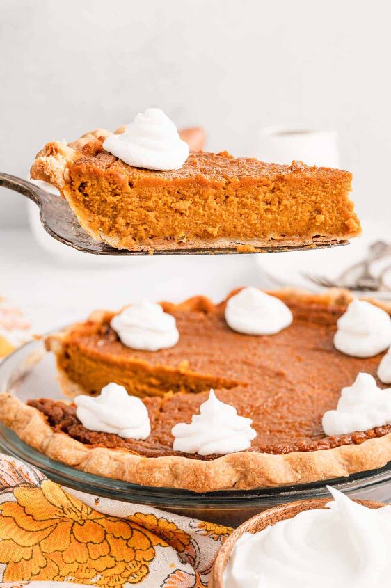 southern sweet potato pie recipe, A piece of sweet potato pie being lifted away from the full pie by a serving spatula and the piece is topped by a dollop of whipped cream