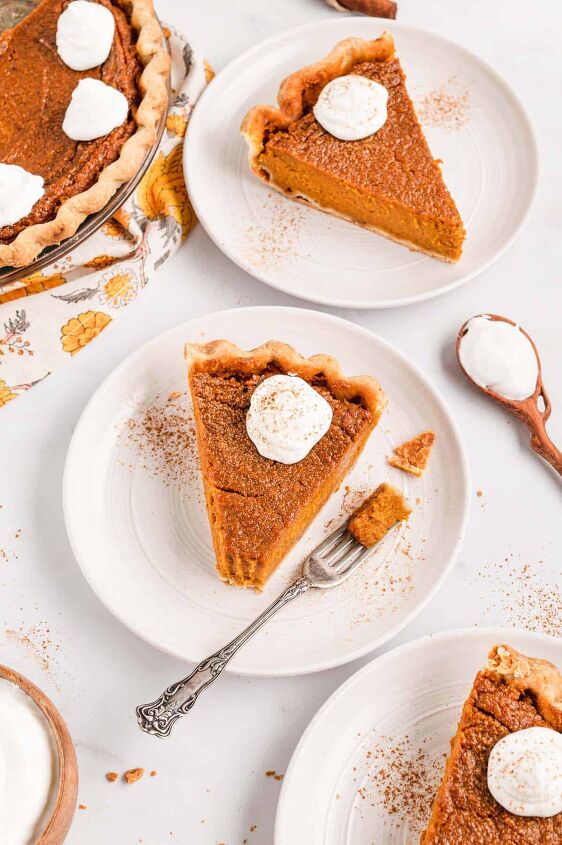 southern sweet potato pie recipe, Three pieces of sweet potato pie on white plates topped with dollops of whipped cream with the rest of the pie on the side
