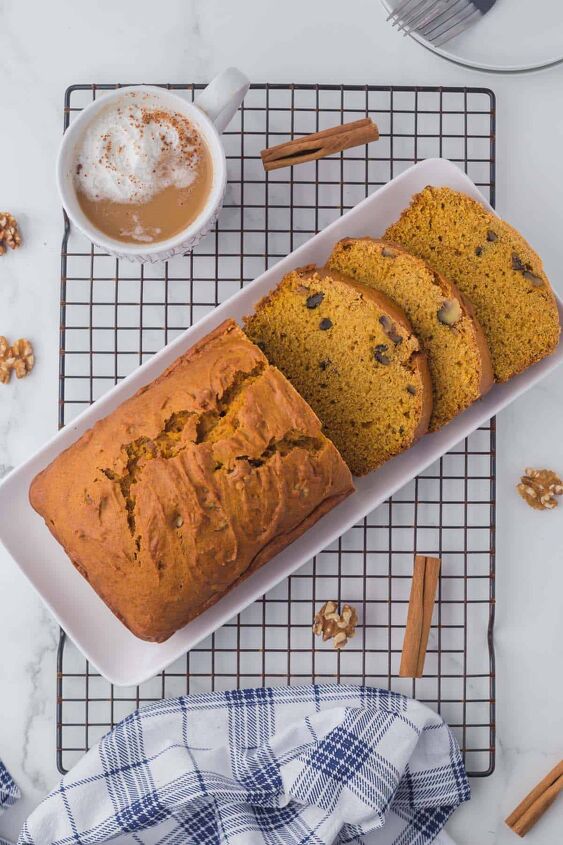 moist pumpkin bread, A pumpkin loaf that has three pieces sliced and laying in front on a white platter sitting on a wire rack with a coffee on the side