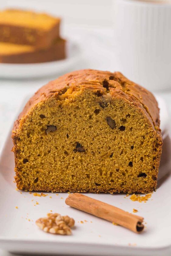 moist pumpkin bread, A loaf of moist Pumpkin bread that has been sliced to see the crumb and walnuts in the bread with a walnut and cinnamon stick in front of it on a white platter