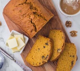 moist pumpkin bread, A pumpkin loaf that has three pieces sliced and laying in front on a wooden cutting board with a small white bowl of pats of butter and a mug of coffee on the side