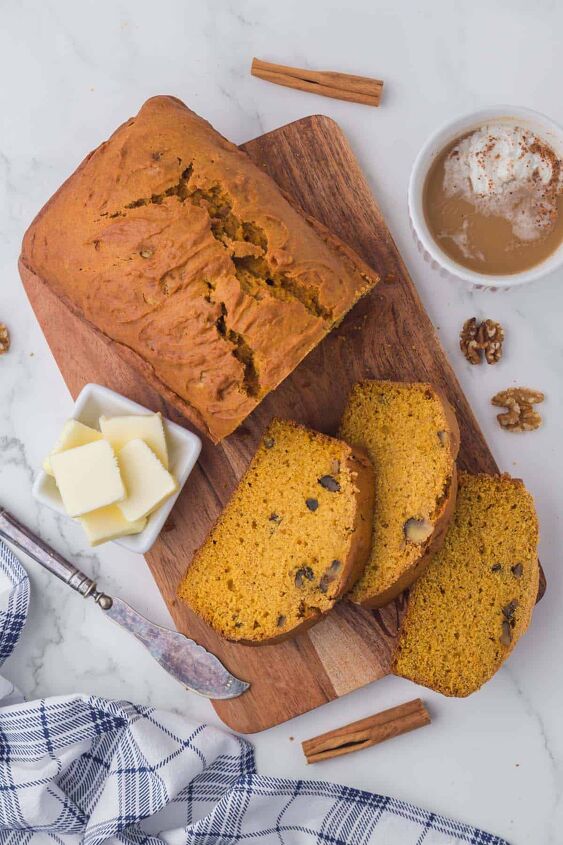 moist pumpkin bread, A pumpkin loaf that has three pieces sliced and laying in front on a wooden cutting board with a small white bowl of pats of butter and a mug of coffee on the side