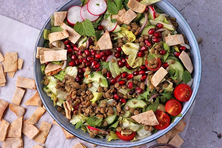 lentil pomegranate salad with tahini dressing, Salad in a blue bowl with lentils pomegranate pita chips lettuce tomatoes cucumbers and herbs