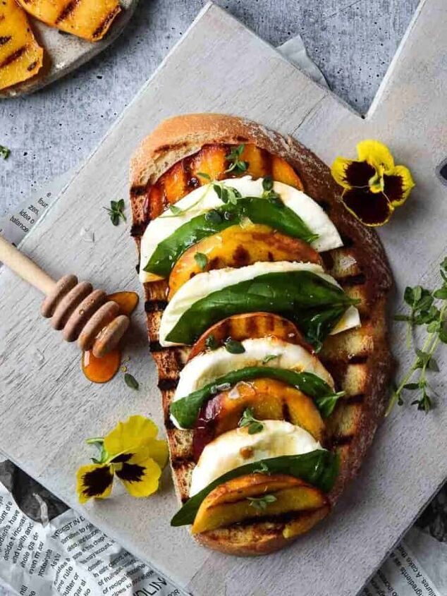 cream cheese avocado toast, Overhead view of toast with grilled peaches on it layered with mozzerella basil and balsamic vinegar on a grey cutting board
