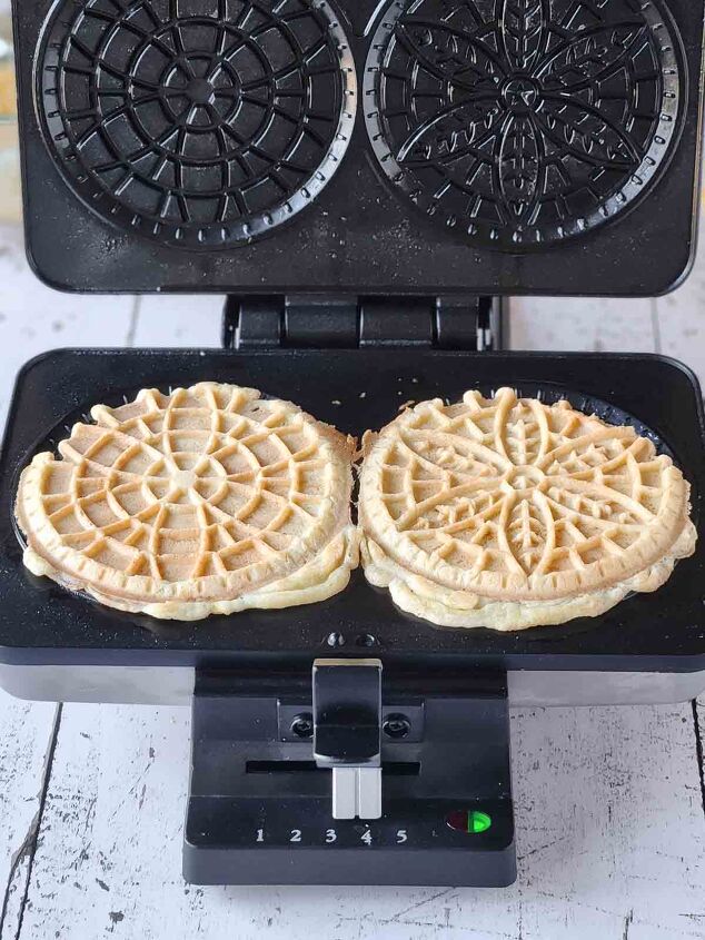 easy lemon pizzelle italian waffle cookies, Two cooked pizzelles in a pizzelle maker with the lid open