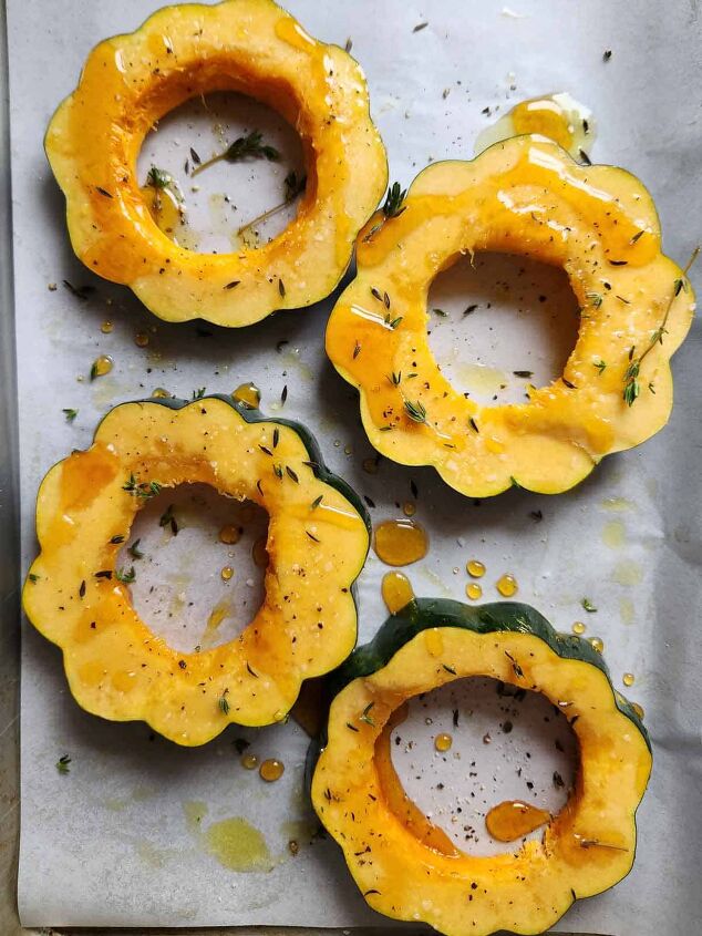 acorn squash egg in a hole with hot honey and thyme, Four acorn squash rings drizzled with honey and seasonings on a baking sheet