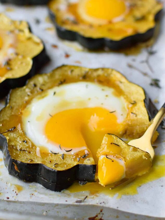 acorn squash egg in a hole with hot honey and thyme, Angled view of acorn squash egg in a hole with a fork bit taken out and dripping yolk