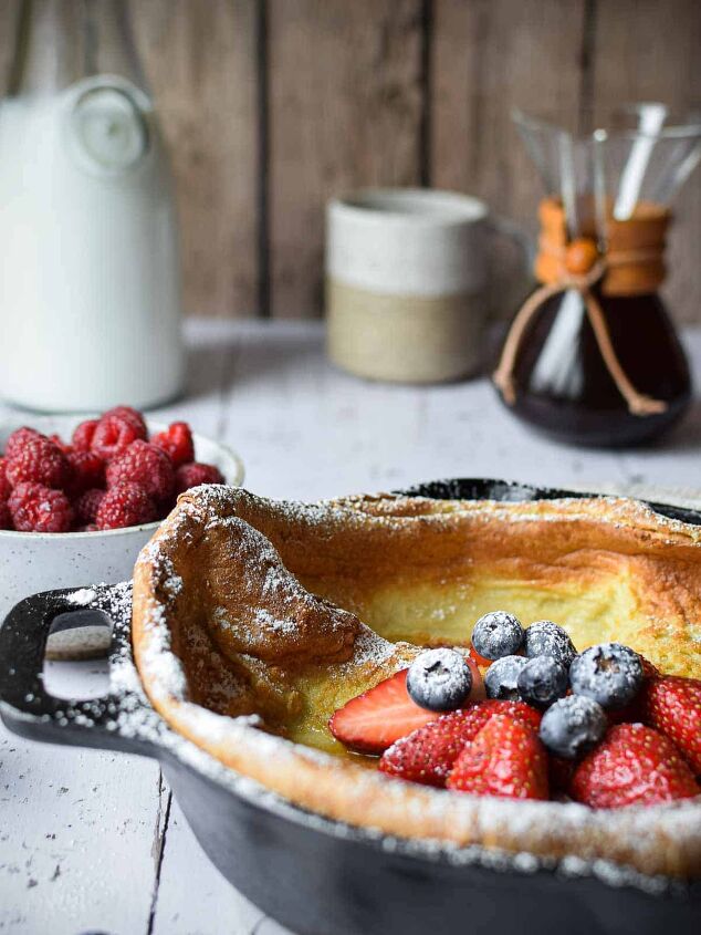 sweet vanilla dutch baby pancake, Eye level view of a Dutch baby in a cast iron skillet with fruit and coffee in the background