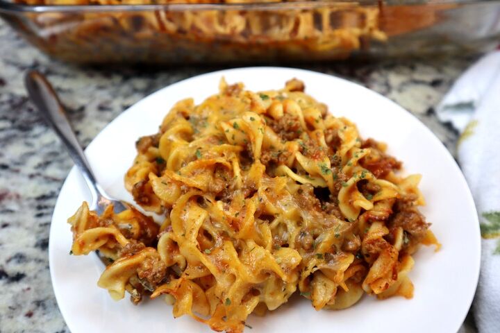 easy cheesy beef noodle casserole recipe, beef noodle casserole in glass dish served with bamboo spoon