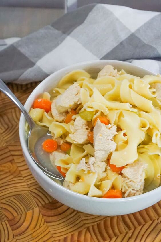 slow cooker chicken noodle soup, Slow Cooker Chicken Noodle Soup in a white bowl with a spoon in it on a brown table next to a gray and white checkered cloth