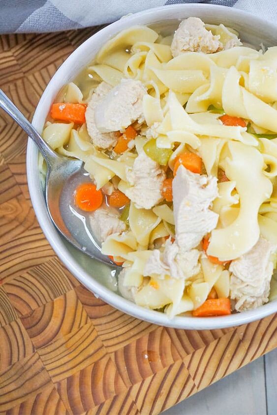 slow cooker chicken noodle soup, Slow Cooker Chicken Noodle Soup in a white bowl with a spoon in it on a brown table next to a gray and white checkered cloth