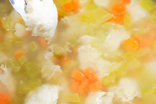slow cooker chicken and dumplings, dumplings being dropped from a spoon into a bowl of chicken soup