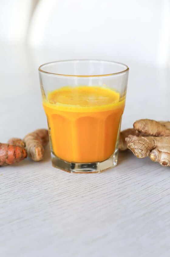 lemon ginger turmeric shot, glass filled with lemon ginger turmeric shot with ginger and turmeric roots