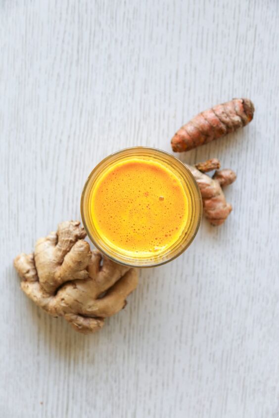 lemon ginger turmeric shot, glass filled with lemon ginger turmeric shot with ginger and turmeric roots from above