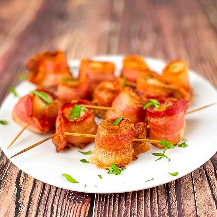 air fryer bacon wrapped scallops, The cooked scallops wrapped in crispy bacon on a white plate garnished with chopped parsley