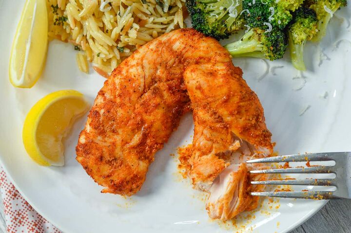 air fryer chicken tenders low carb no breading, Fork cutting air fryer chciken on white plate next to lemon wedge with orzo and broccoli in background