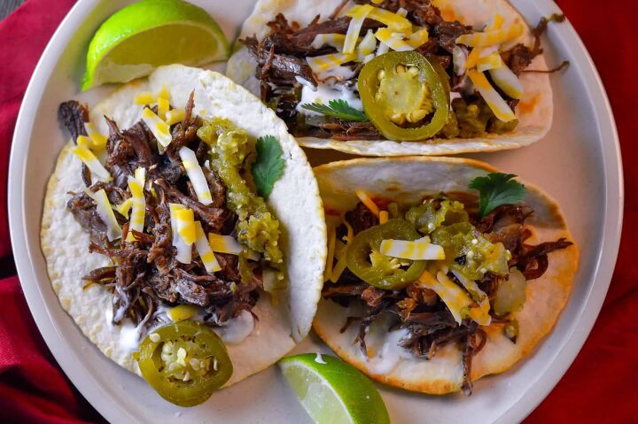 easy instant pot shredded beef multi purpose, 3 Shredded Beef street Tacos with some shredded cheese salsa verde and pickled jalapeno on white plate with lime wedges