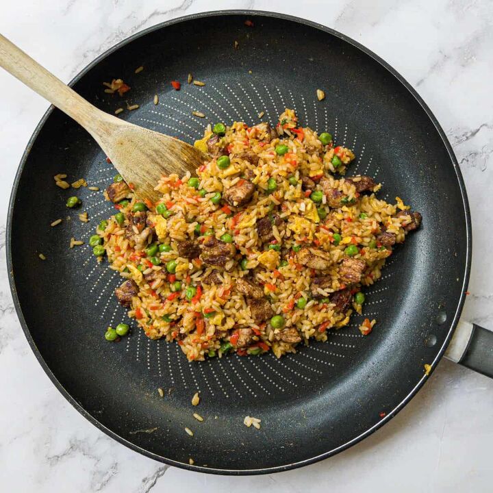 pork belly fried rice, A frying pan containing fried rice that is being stirred with a wooden spoon