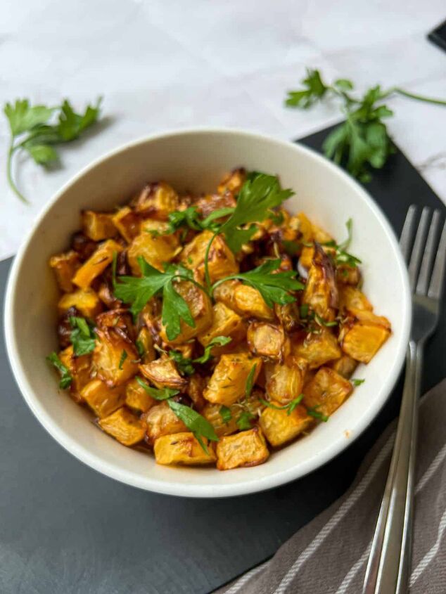 roasted swede oven and air fryer, A bowl of roasted swede cubes garnished with fresh parsley There is a fork and some fresh parsley in the background