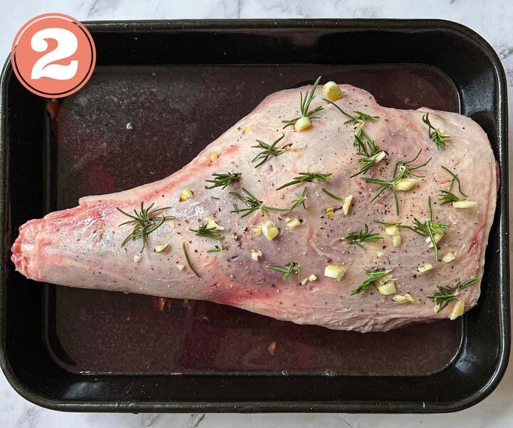 slow cooked leg of lamb in red wine, A raw leg of lamb studded with garlic and rosemary sitting in a roasting tin