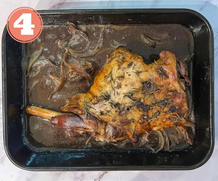 slow cooked leg of lamb in red wine, A leg of lamb lying in gravy garnished with rosemary in a roasting tin