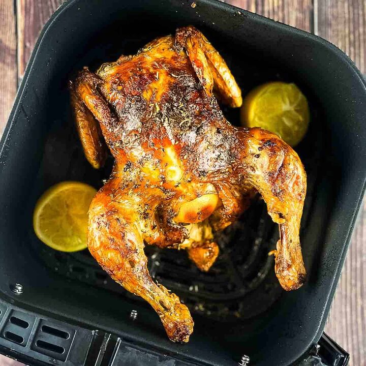air fryer whole roast chicken with lemon and garlic, Golden brown whole chicken with crispy skin in an air fryer basket garnished with lemon wedges and fresh herbs