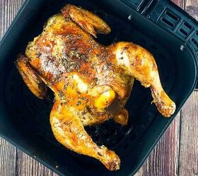 air fryer whole roast chicken with lemon and garlic, Golden brown whole chicken with crispy skin in an air fryer basket garnished with fresh herbs
