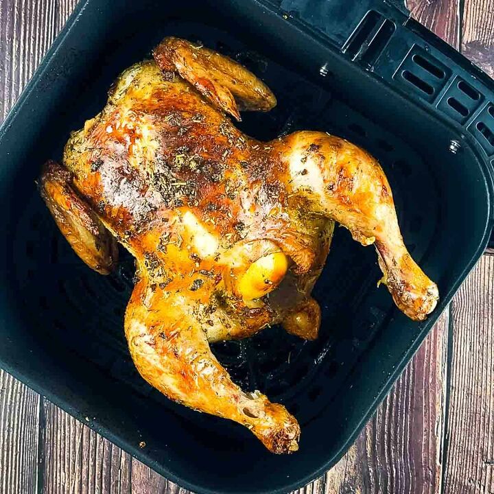 air fryer whole roast chicken with lemon and garlic, Golden brown whole chicken with crispy skin in an air fryer basket garnished with fresh herbs