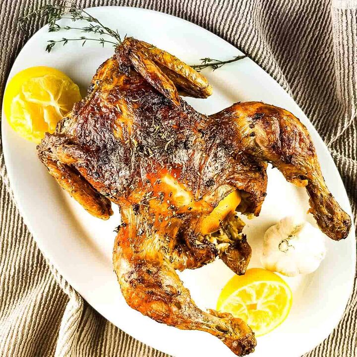 air fryer whole roast chicken with lemon and garlic, The roast chicken on a serving platter with lemon wedges and fresh thyme