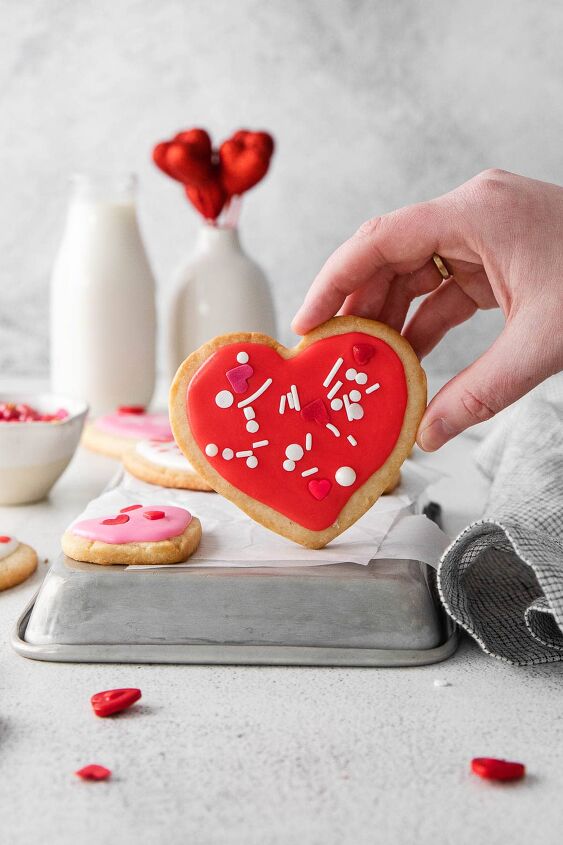 iced shortbread cookies, heart shaped red frosted shortbread cookies being held by a woman s hand