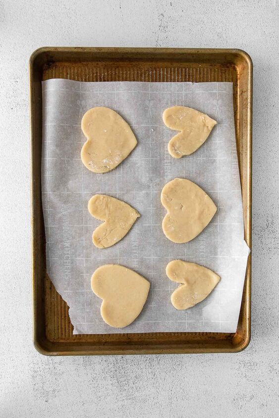 iced shortbread cookies, six heart shaped shortbread cookies on parchment paper lined baking sheet