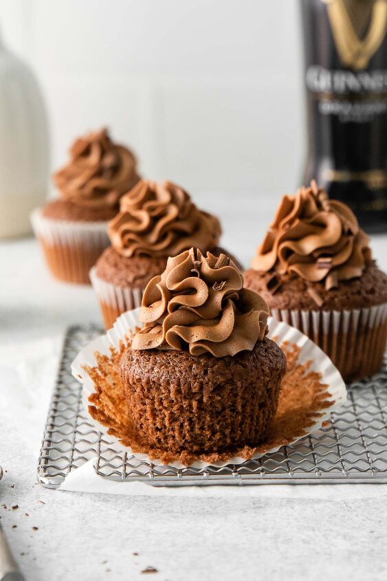 guinness chocolate cupcakes, three guinness chocolate cupcakes with chocolate frosting on a wire rack with the white liner pulled back