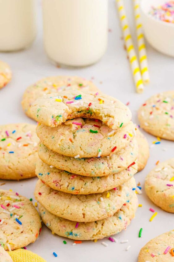 funfetti cake mix cookies, A tall stack of funfetti cake mix cookies from the side on a counter with the top cookie missing a bite and more cookies scattered around the counter