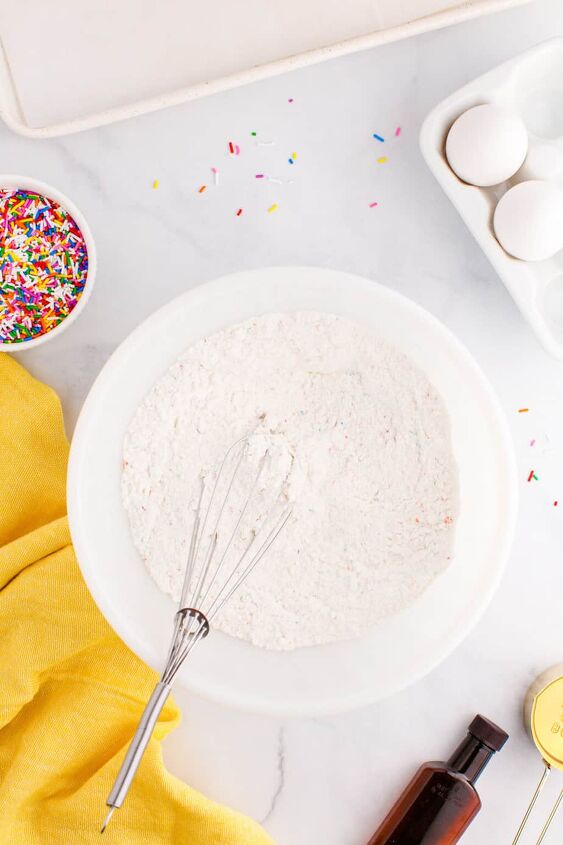 funfetti cake mix cookies, A whisk mixing dry ingredients for funfetti cookies in a bowl from overhead