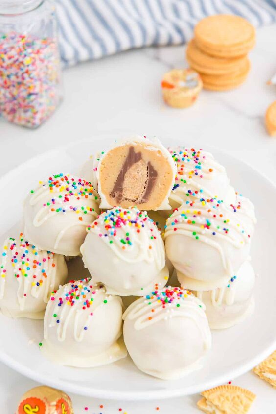 peanut butter cup stuffed truffles, A plate of white chocolate truffles topped with sprinkles with a bite taken out of the top one showing a peanut butter cup inside