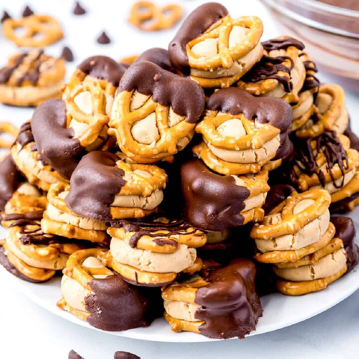 peanut butter cup stuffed truffles, Peanut butter stuck between small pretzels dipped in chocolate stacked high on a plate from the side on a counter