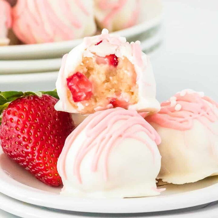 peanut butter cup stuffed truffles, Close up of a strawberry shortcake truffle missing a bite showing strawberry bits inside on top of a few more truffles and a fresh strawberry on a plate