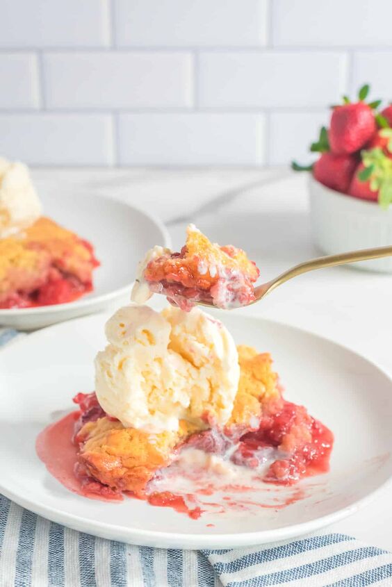 fresh strawberry cobbler, A fork full of strawberry cobbler and ice cream being scooped from a plate on a counter from the side