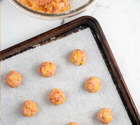 sausage and cheese balls, A glass mixing bowl with dough for sausage cheese balls in it There is a dough scoop in the bowl Next to it is a parchment lined baking sheet with balls of the sausage mixture on it