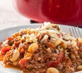 cheesy goulash recipe, white plate full of american goulash with ground beef elbow noodles and diced tomatoes topped with shredded cheese